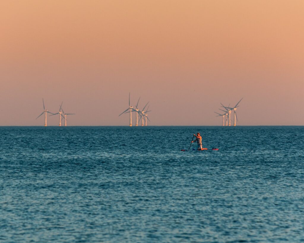 Lone swimmer facing a floating offshore wind farm in the background