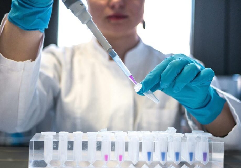 Woman in a lab coat and wearing gloves while holding a pipette